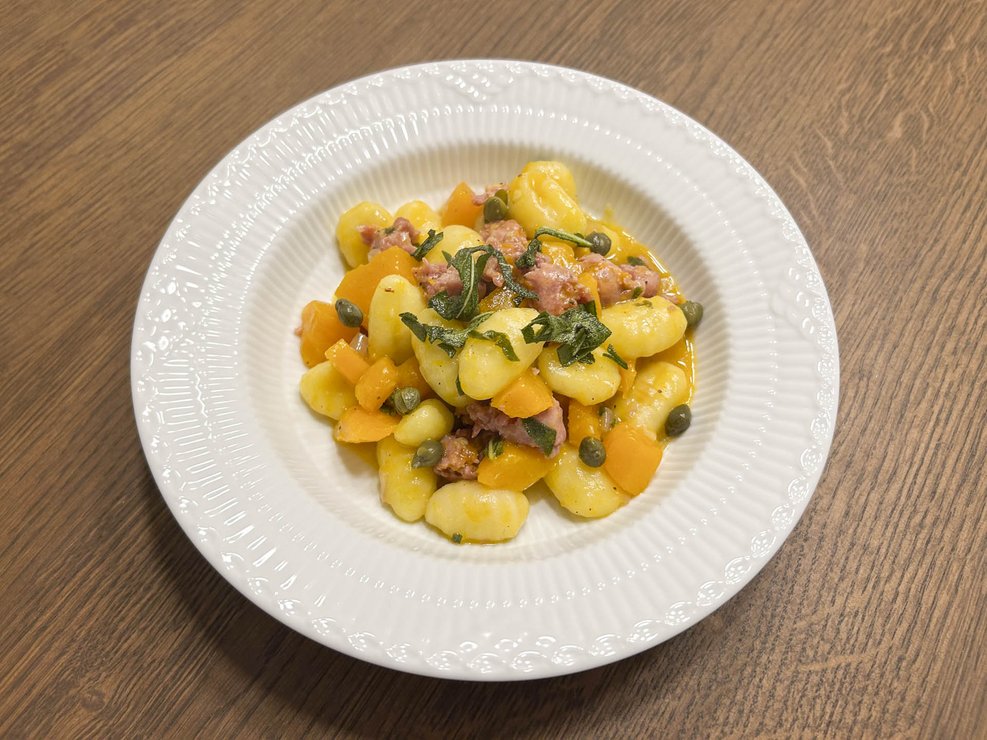 Den færdige servering af gnocchi i efterårsklæder med græskar, salvie og salsiccia