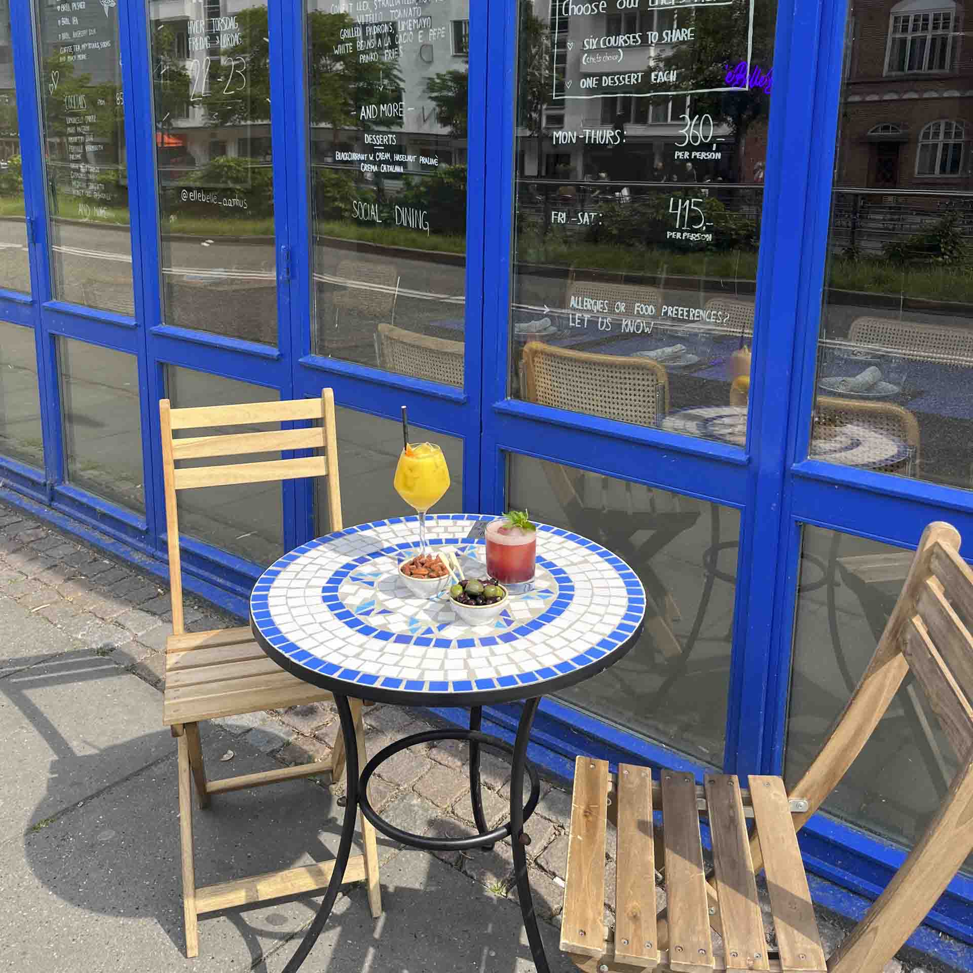 Mosaikbord og træstole foran den blå facade hos Elle Belle ved åen i Aarhus