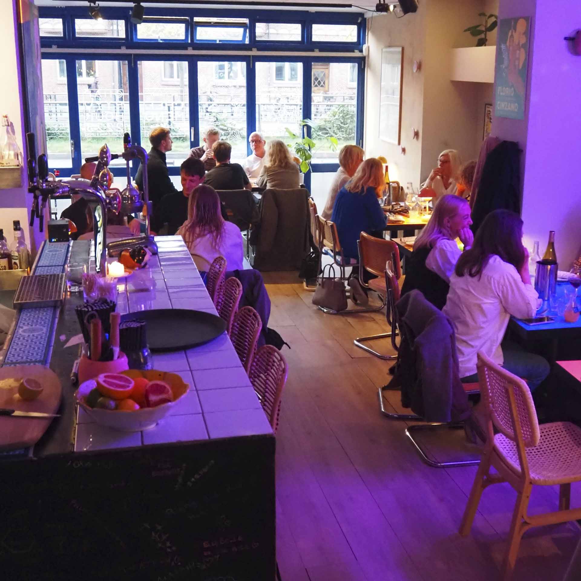Gæster ved bordene i lilla lys hos Elle Belle ved åen i Aarhus