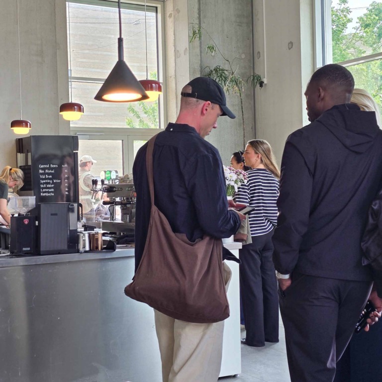 G&aelig;ster i k&oslash; ved disken hos F&aelig;tter p&aring; Godsbanen, med tavle over drikkevarer og store vinduespartier i baggrunden.