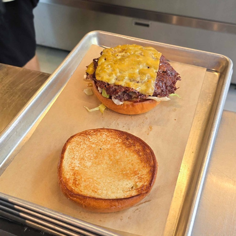 Smash burger under samling med b&oslash;f og smeltet ost, ristet topl&aring;g ved siden af, hos Aarhus Smash.