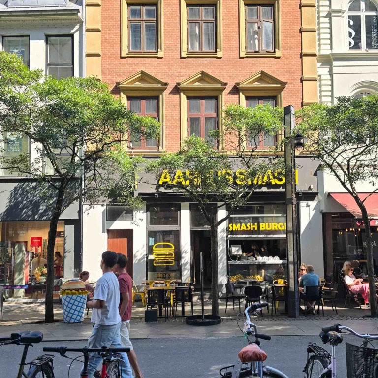 Facaden af Aarhus Smash p&aring; Immervad med udeservering og g&aelig;ster p&aring; fortovet i solskin.