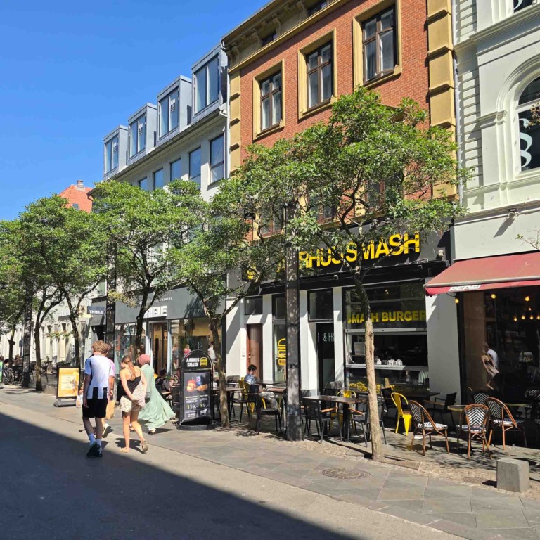 Facaden af Aarhus Smash p&aring; Immervad med udeservering og g&aelig;ster p&aring; fortovet i solskin.