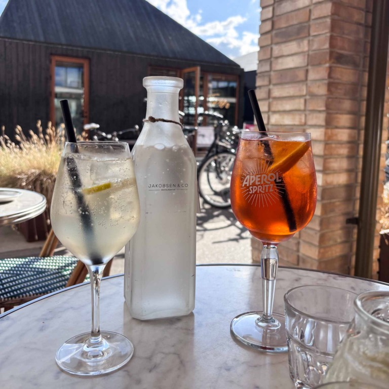 Aperol Spritz og hvidvinsdrink p&aring; marmorbord ved Jakobsen & Co, med vandflaske mellem glassene.