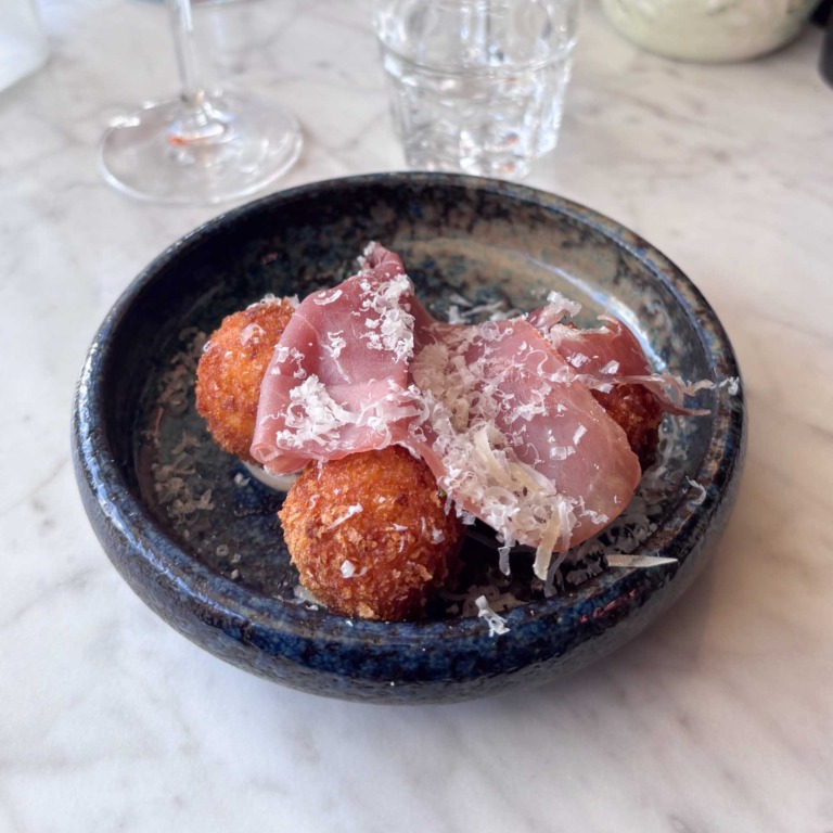 Friturestegte arancini toppet med skinke og revet ost i m&oslash;rkeglaseret sk&aring;l hos Piccolo Aarhus &Oslash;.