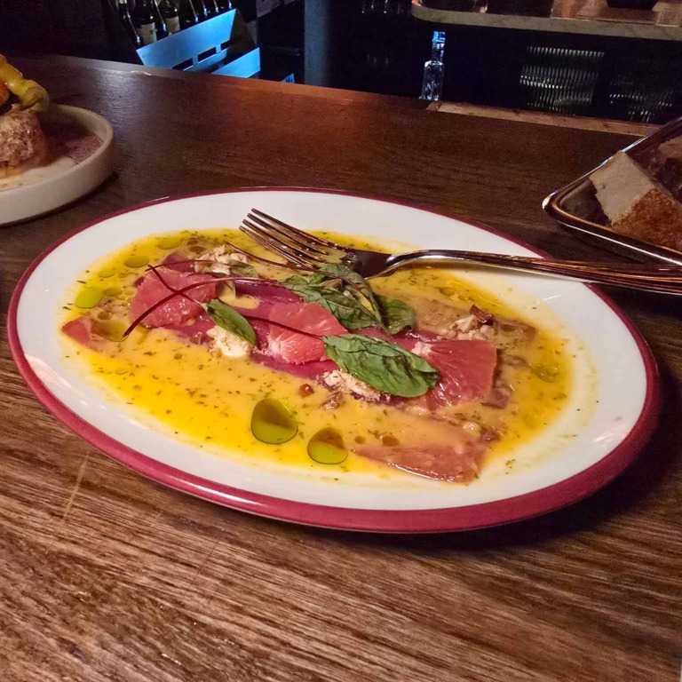 Carpaccio p&aring; en hvid tallerken med r&oslash;d kant hos Boca R&eacute;al