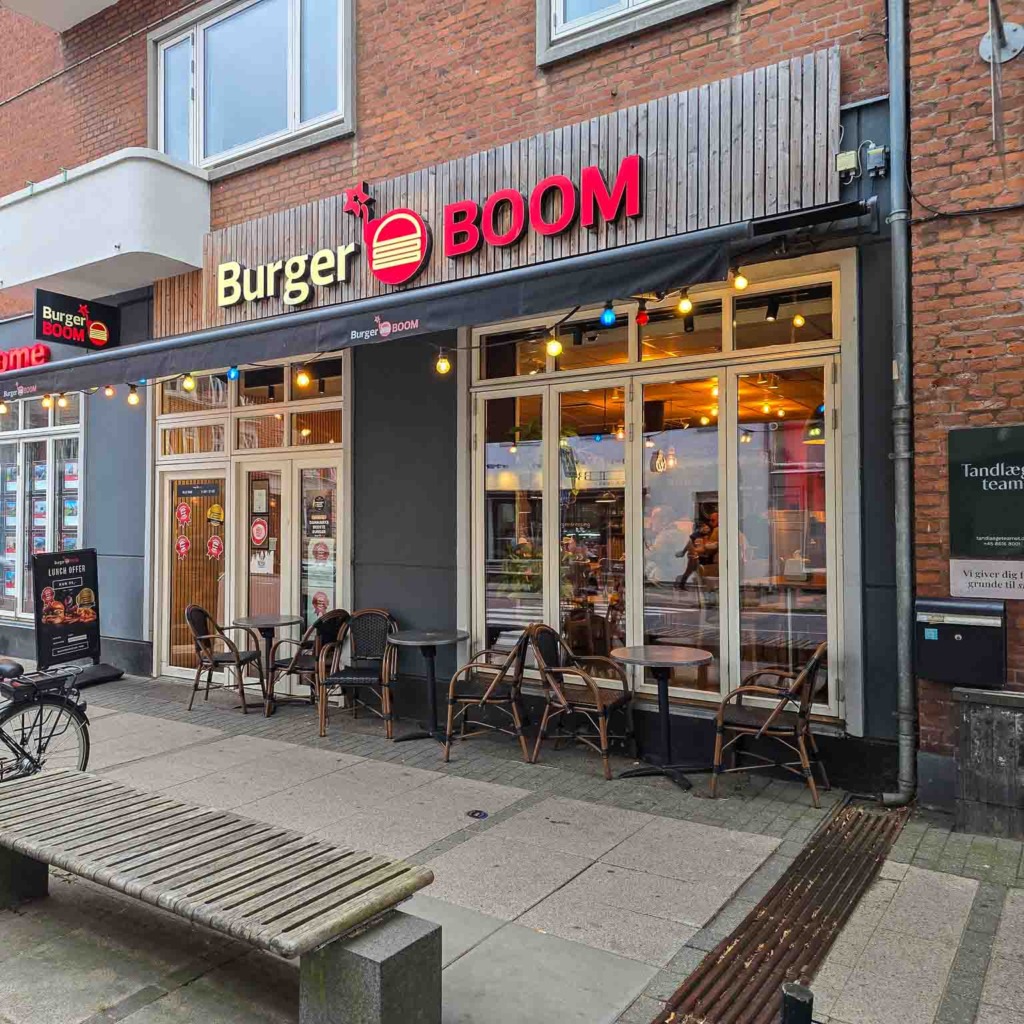 Facaden med rødt skilt og bænk foran hos Burger Boom på Trøjborg