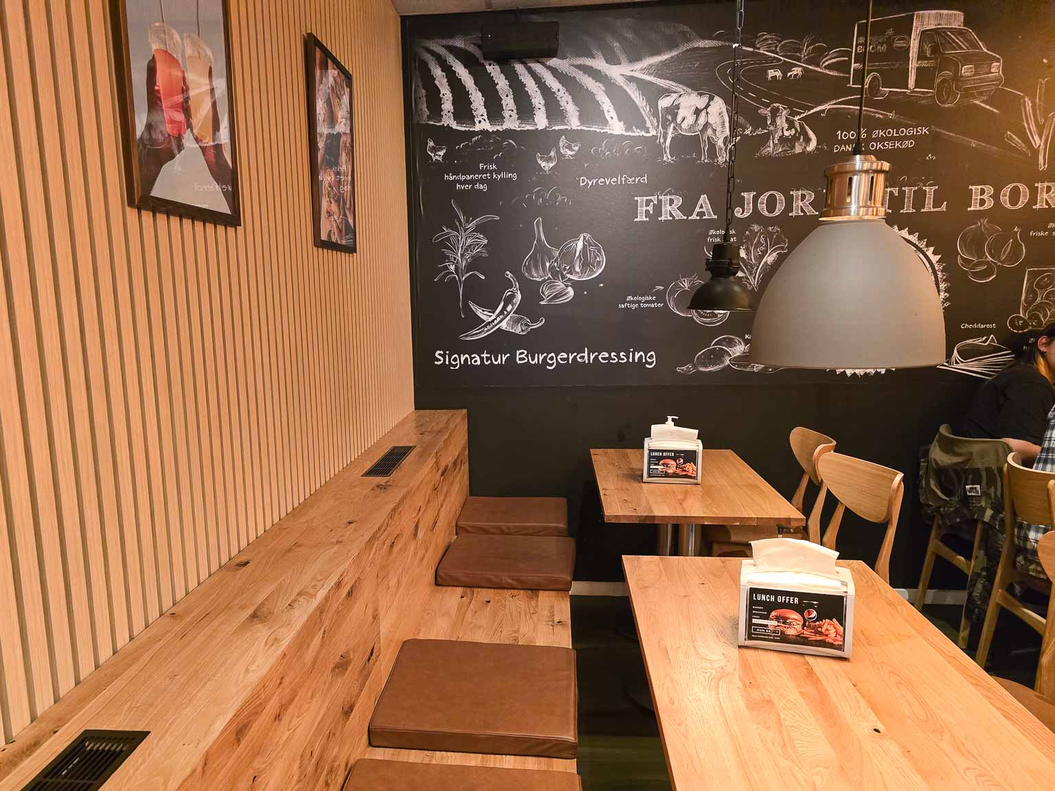 Træbænke og borde under tavlevæg hos Burger Boom på Trøjborg