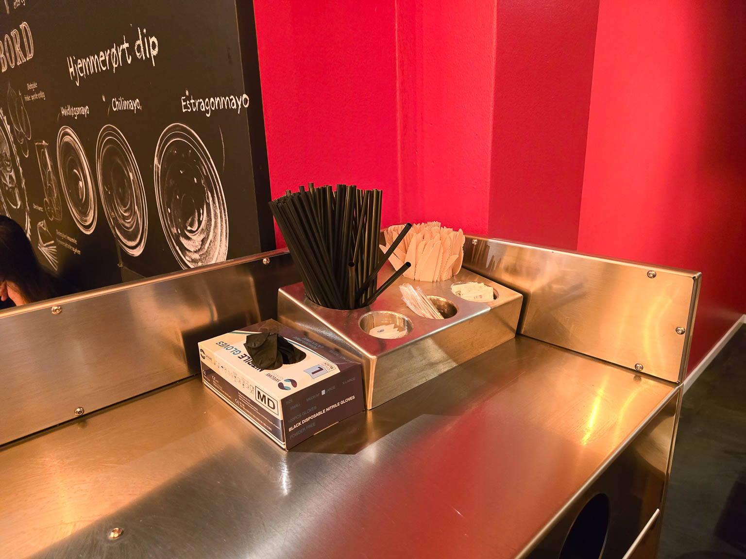 Station med sugerør og servietter ved rød væg hos Burger Boom på Trøjborg