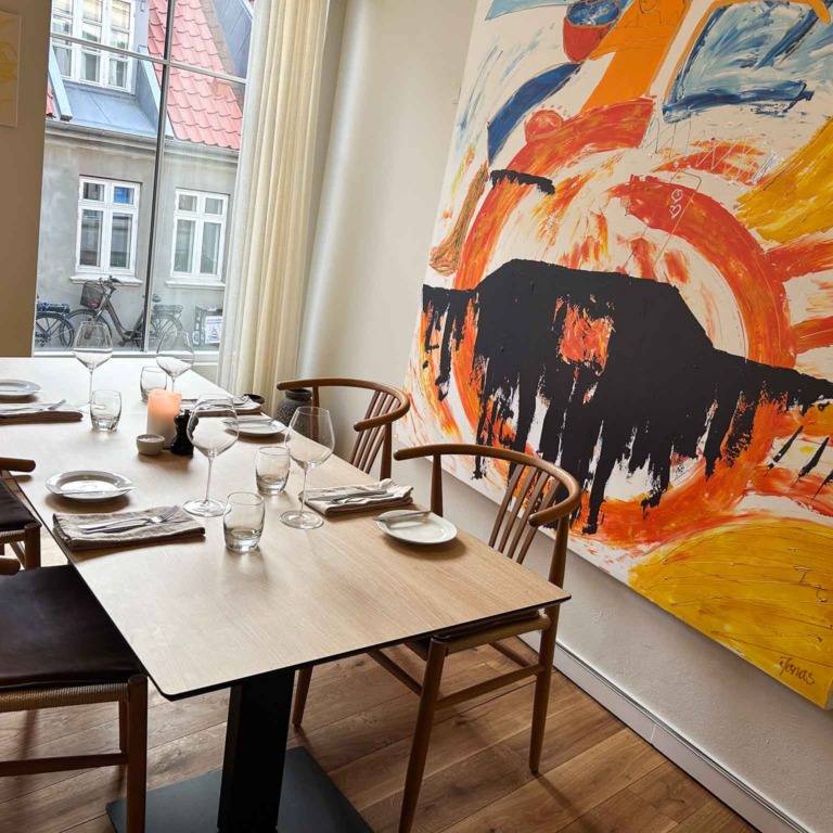 Bord ved vinduet og et stort maleri hos Restaurant Ukurant i Mejlgade i Aarhus