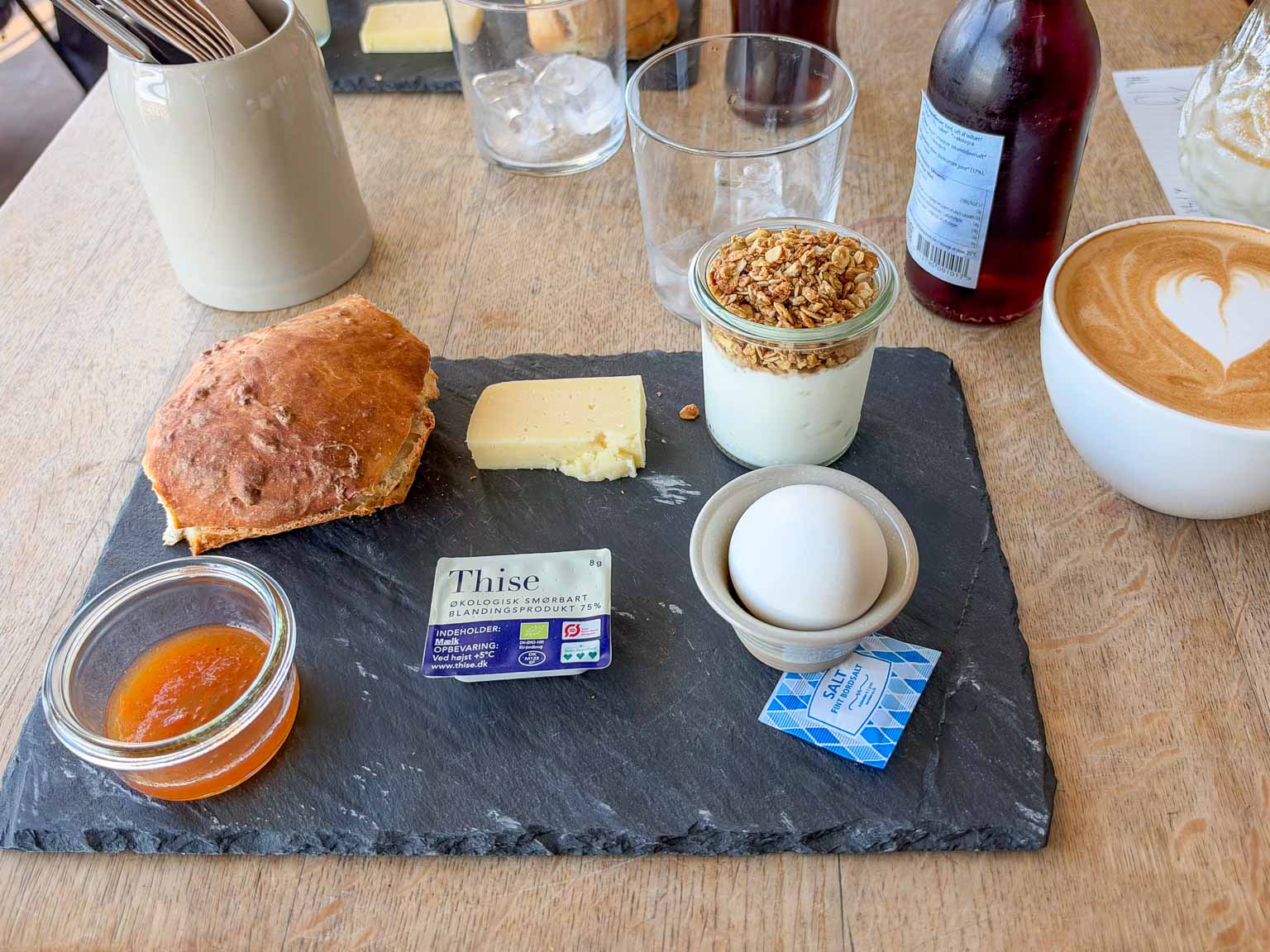 Morgenmad med bolle, ost, kogt æg, granola og marmelade på skiferplade